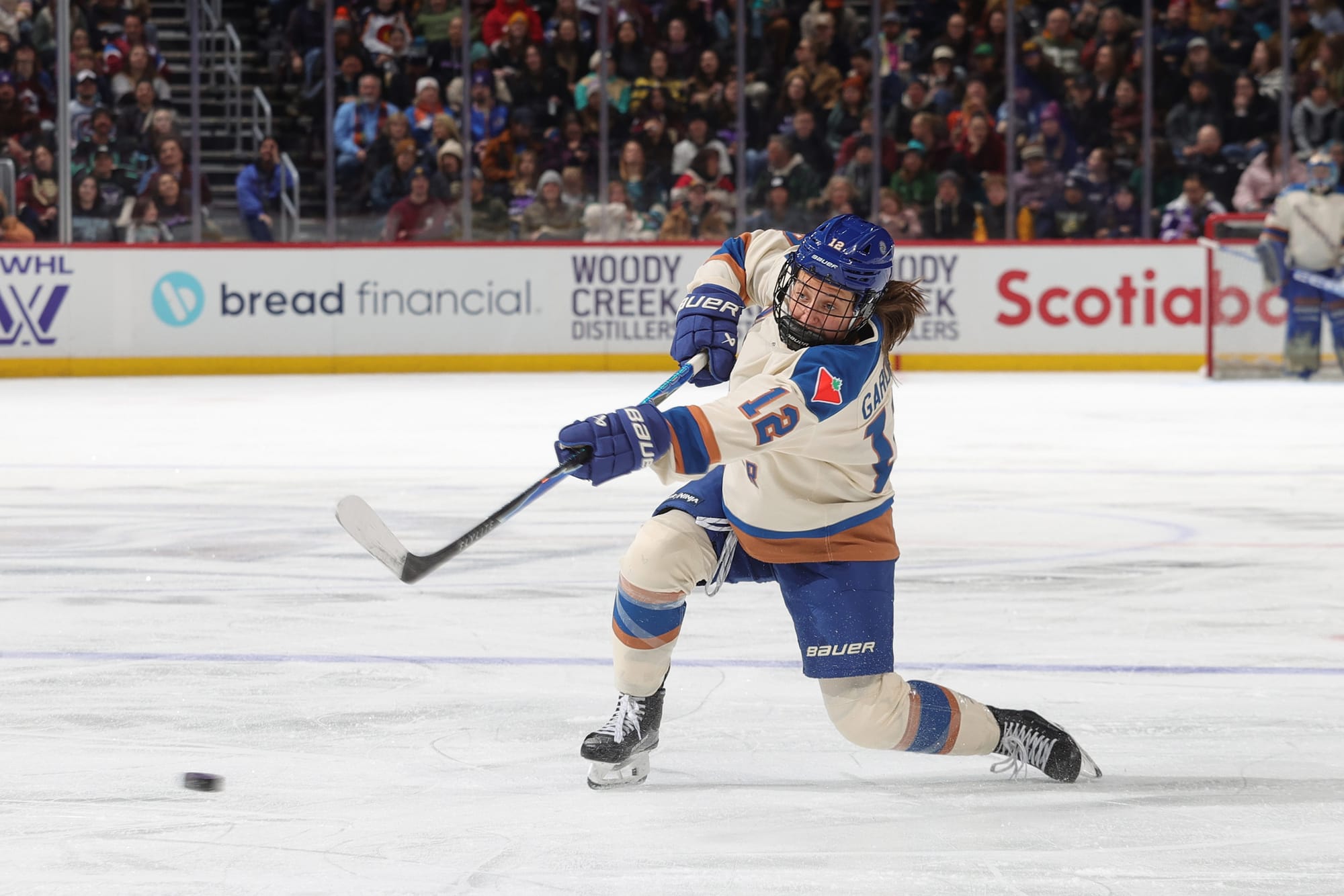 Gardiner leans forward as she drops to one knee and follows through on a hard shot from the blue line. She is wearing a cream away uniform.