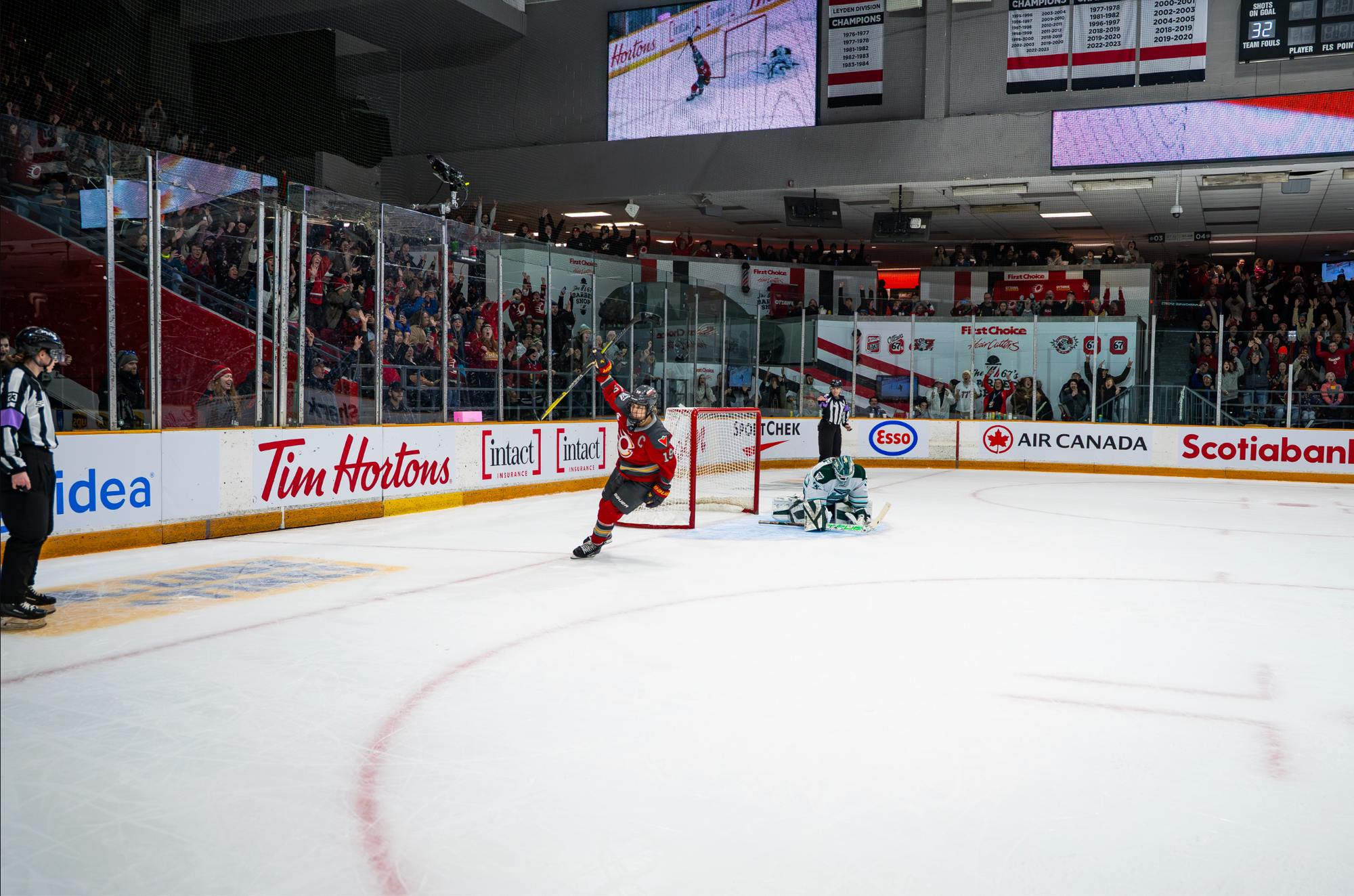 Jenner raises her stick in celebration after scoring a shootout goal. Aerin Frankel is on her knees in the background. Jenner is wearing a red home uniform, while Frankel is in a white away one.