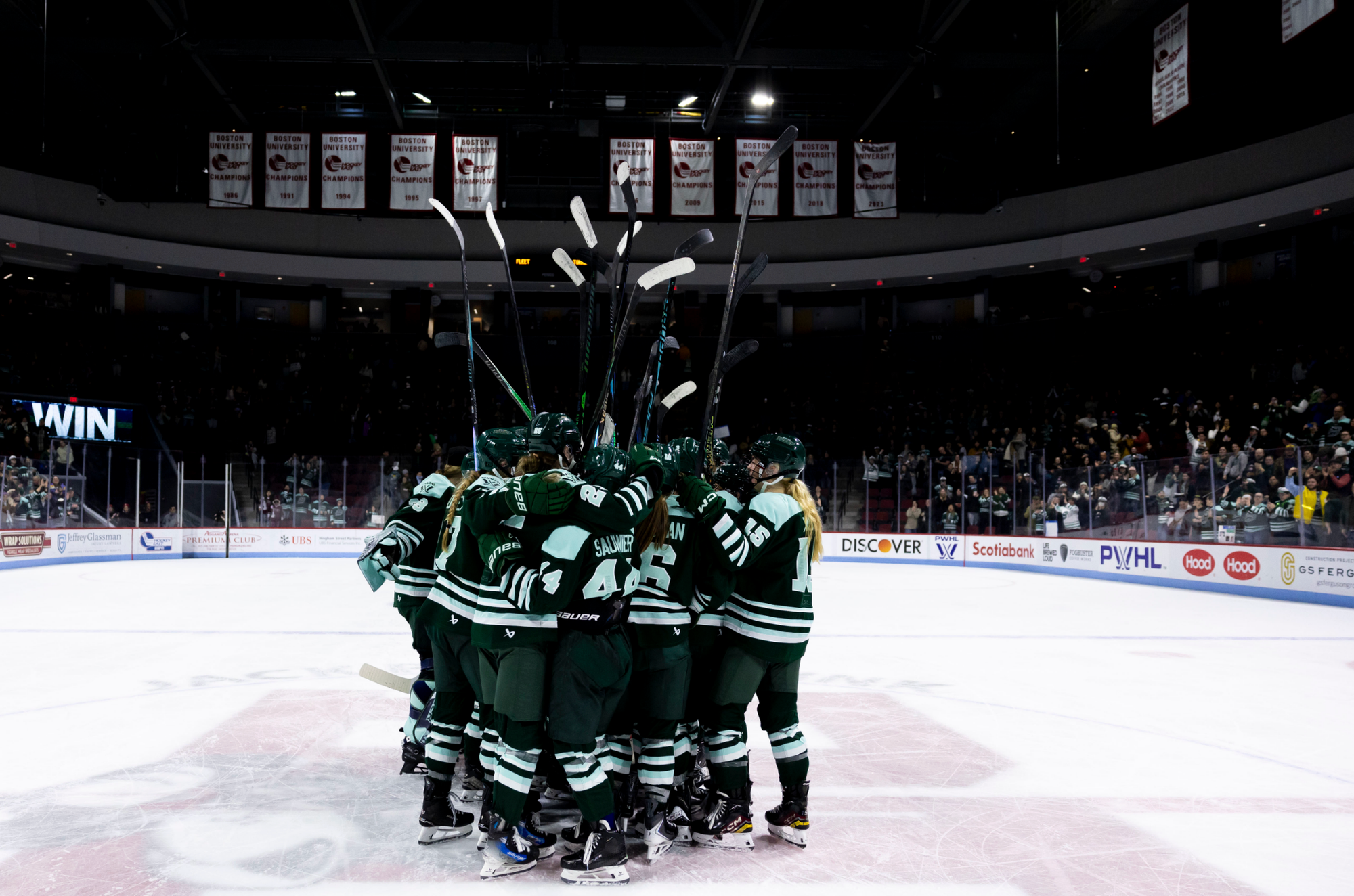 The Fleet celebrate their win with a tight, sticks raised group hug at center ice. They're wearing green home uniforms.