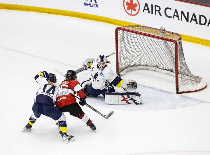 A Scotiabank and Adidas player battle in front of Adidas goaltender Aerin Frankel who is stretched out infront of her net.