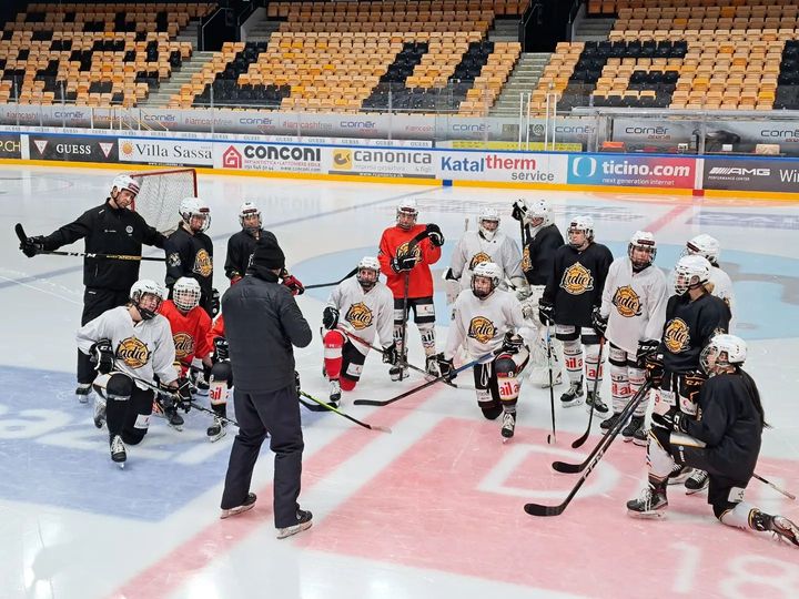 Hockey players in practice jerseys stand and kneel around a coach