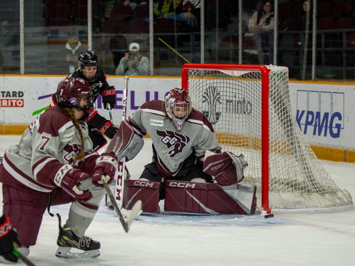 Carleton and uOttawa players chase a puck in front of goalie Mahika Sarrazin.