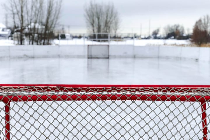 The view from behind a hockey net of an outdoor hockey rink.