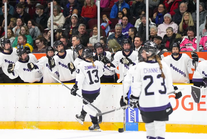 Grace Zumwinkle and her teammates, wearing their white away uniforms, celebrate her goal at the bench.