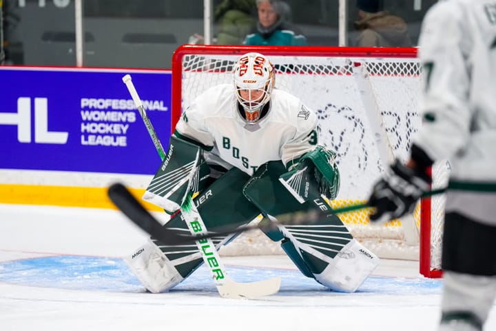 Emma Söderberg, wearing a white jersey, green pads, and a UMD mask, prepares to make a save during warm-ups of a prior game.