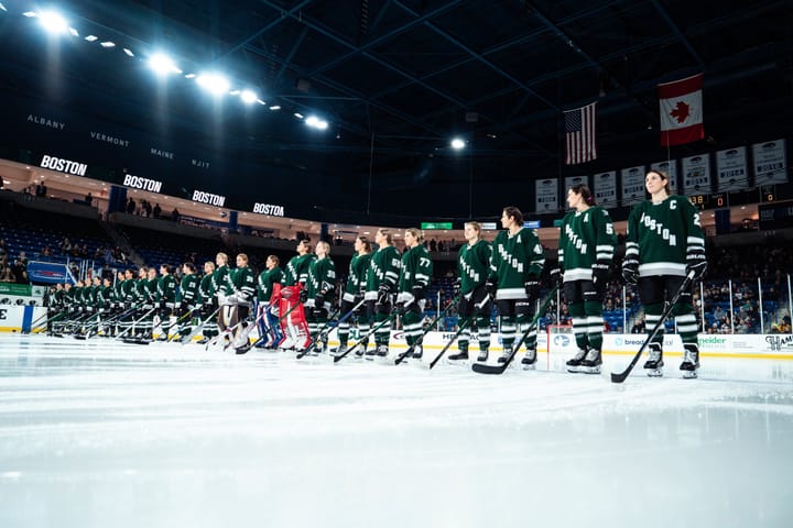 A photo of PWHL Boston lined up on the blueline during their home opener. They are all wearing their green home uniforms.