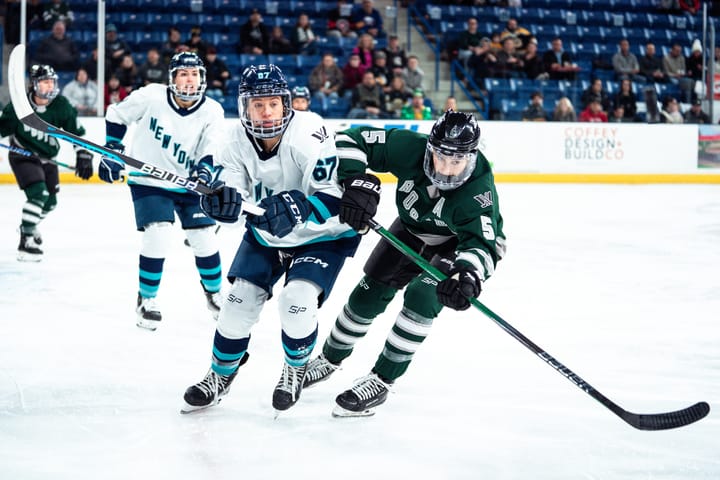 Megan Keller, wearing a green home uniform, and Emma Woods, wearing a white away uniform, battle for positioning.