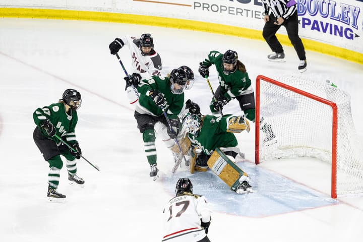 Aerin Frankel, wearing her brown pads, Boston makes, and green home uniform, makes a save through net front chaos. 