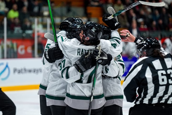 Boston players celebrate a goal against Montréal. They are in a group hug. All are wearing white away uniforms.