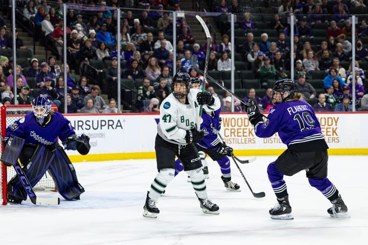 Jamie Lee Rattray calls for the puck in front of the Minnesota goal. She is in white and her stick is raised.