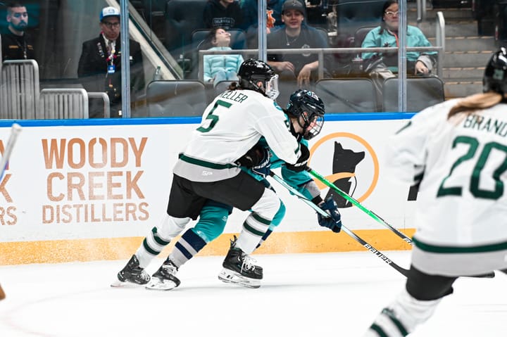 Keller defends a NY player. Keller's body is wrapped around her and she is wearing white, while the NY player is in teal.