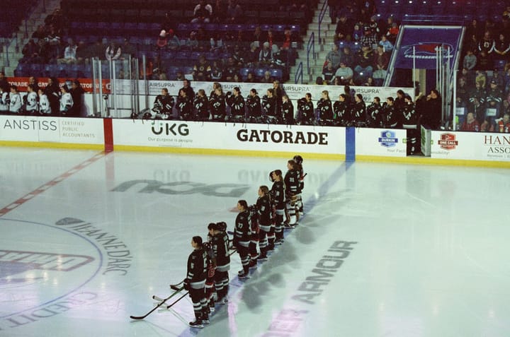 Boston players stand during the national anthem before a game. They are wearing green home uniforms.