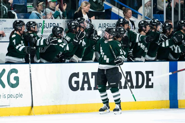 Emily Brown skates down and gets fist bumps at the bench to celebrate her first goal. She is wearing a green home uniform.