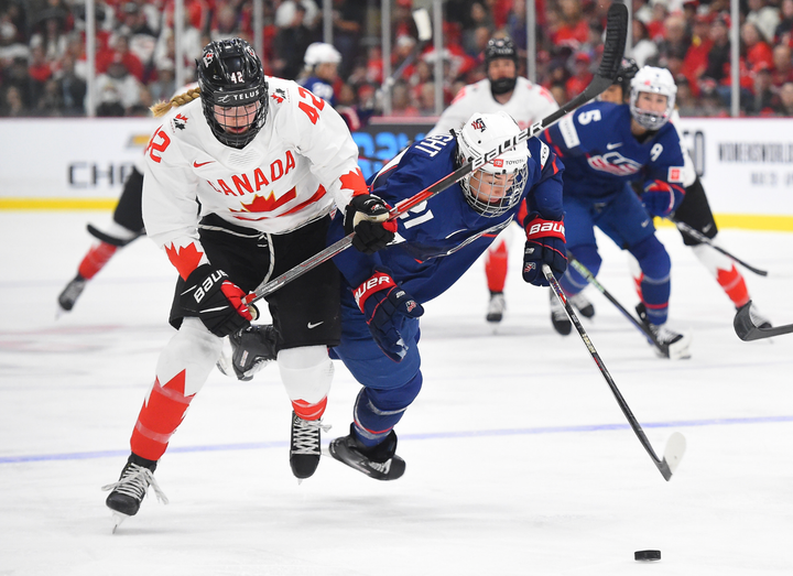 Thompson (left in white) battles Knight (right in blue), who is falling forward, for the puck. Knight currently possesses it.