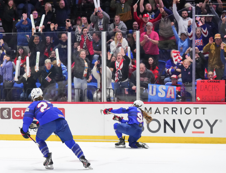 Simms fist pumps while on her knees to celebrate her overtime winner. Heise is to her left. Both are in blue.