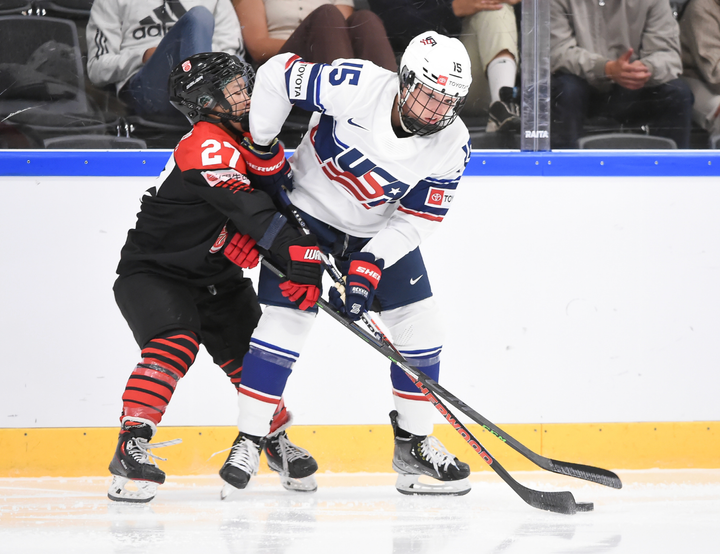 Harmon (right) battles Koyama (left) for the puck. Harmon currently controls it. She's in white, and Koyama is in black/red