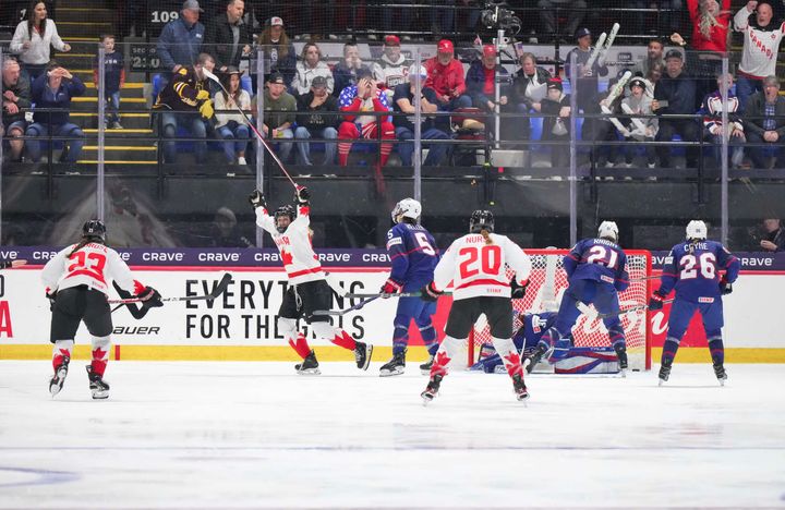 Serdachny raises her arms in celebration. Two of her teammates skate to join her, while three USA players look at their net.