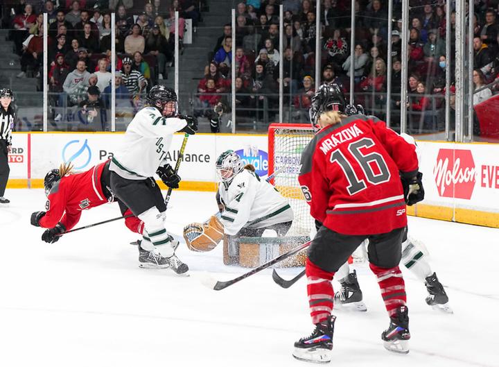 Frankel makes a save from her knees, with a Boston and Ottawa player in front of her and another pair to her left. 