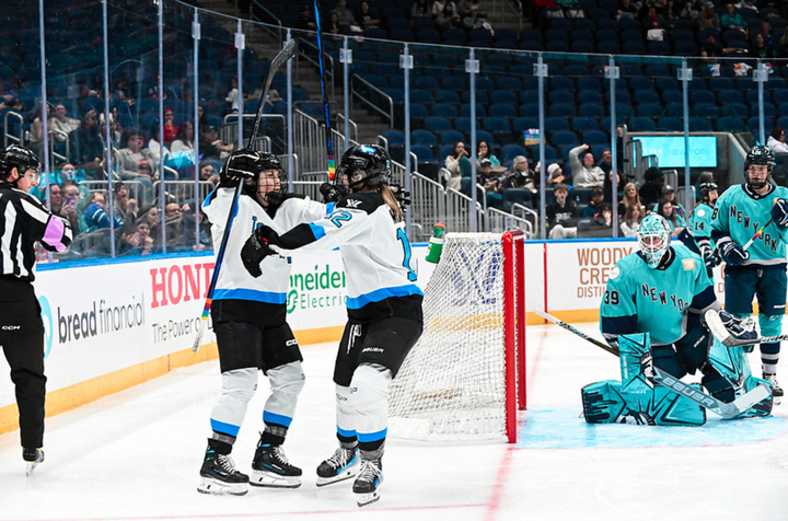 Two Toronto players celebrate a goal against New York with a group hug. They are wearing white away uniforms.