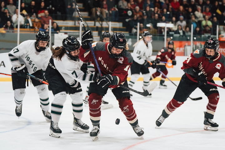 Morin (left in white) reaches around Murphy (right in maroon) to try to get the puck, which is bouncing in front of her.