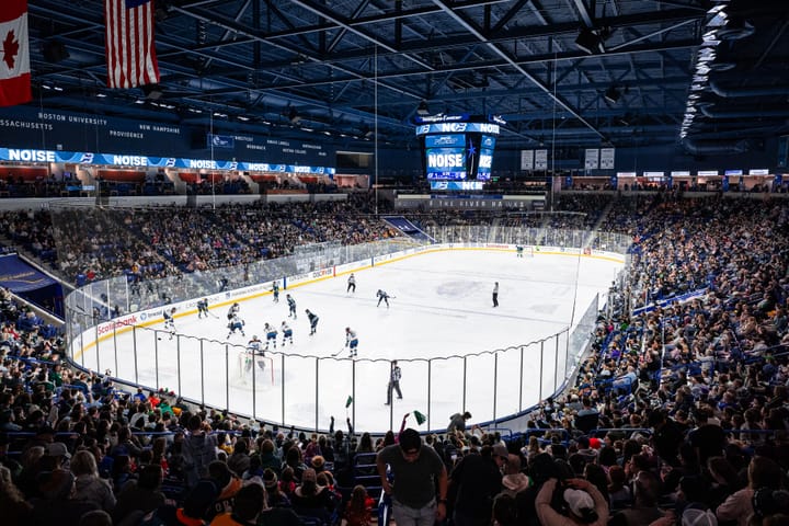 A view from the concourse of the ice as the Fleet and Sirens prepare for a faceoff in the Fleet's offensive zone at the Tsongas Center. The packed crowd is visible all around the ice.