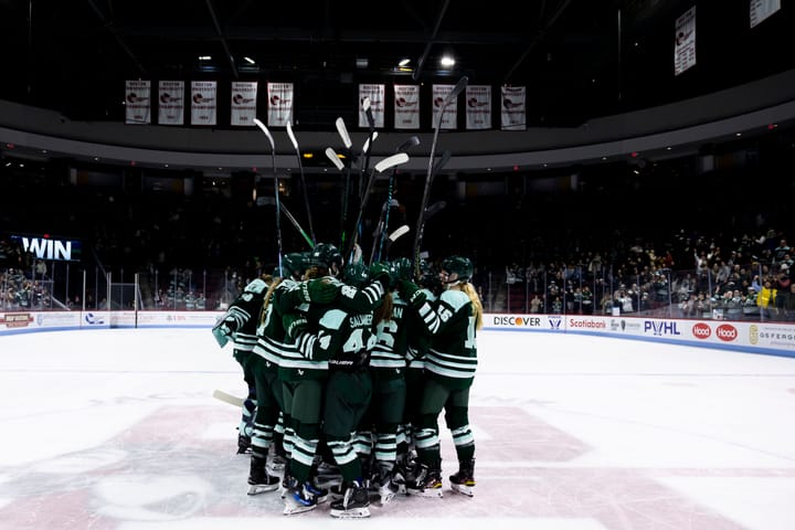 The Fleet celebrate a win with a tight group hug at center ice. They are all wearing green home uniforms.